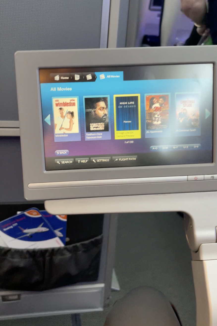 An in-flight entertainment system displays movie options including 