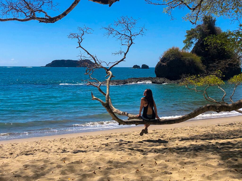 Woman sitting on a low hanging branch over a sandy beach in Costa Rica