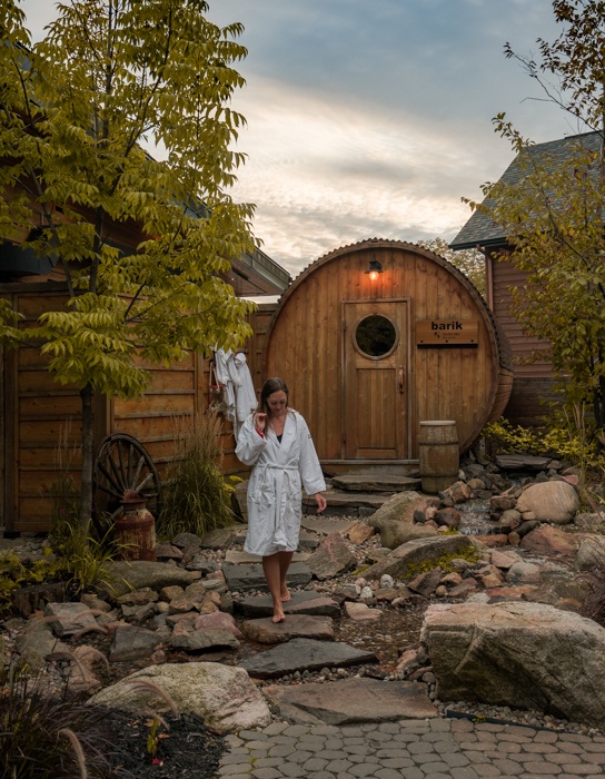 Woman walking across large stones in front of a barrel-shaped wooden building in Quebec