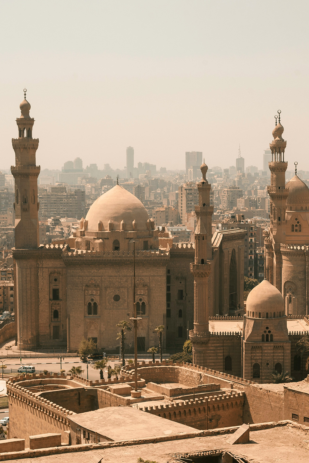 A bird's eye view of the Sultan Hassan Mosque in Cairo shows an enormous building topped with a dome and surrounded by tall minarets.