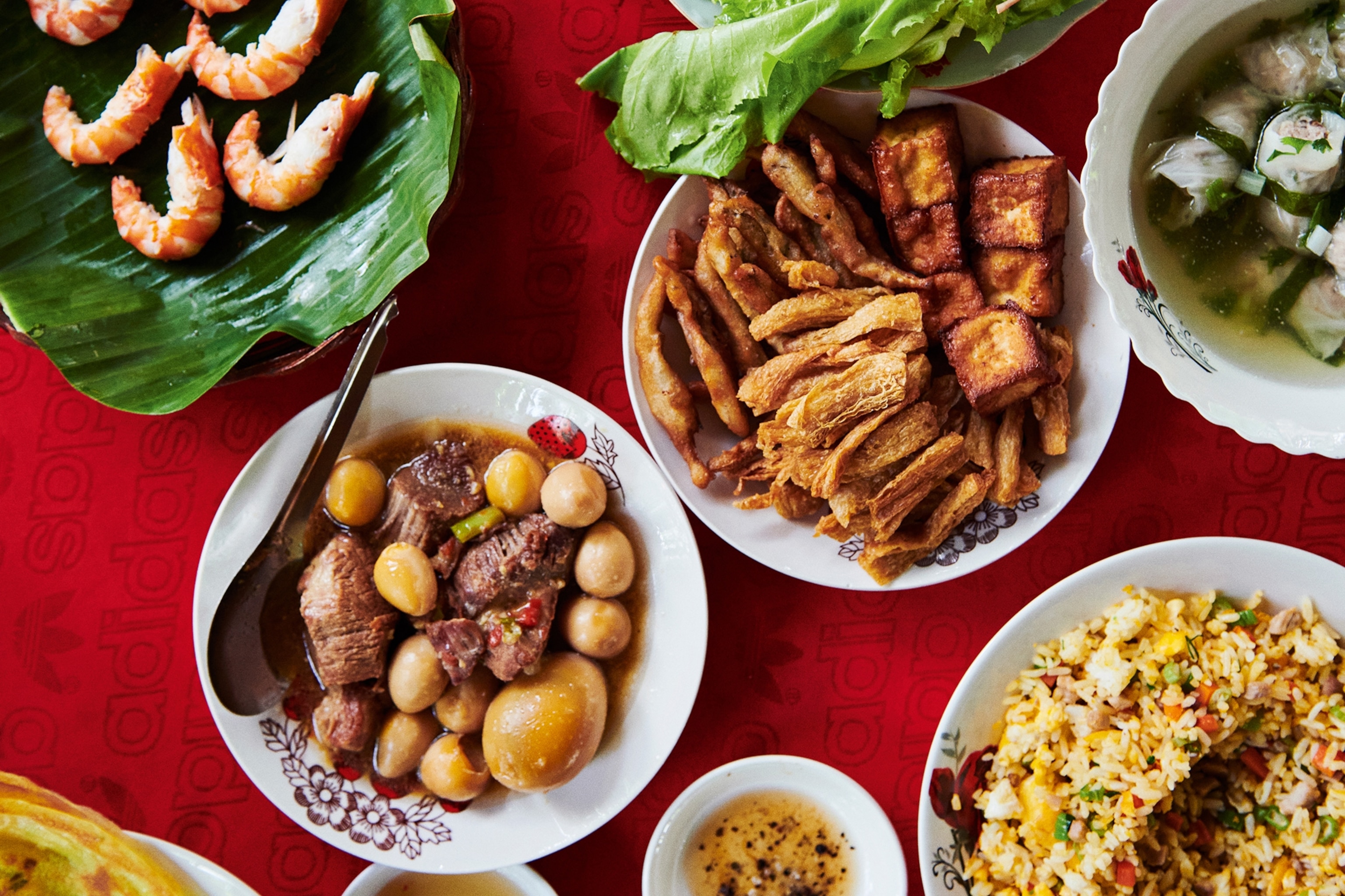 A variety of Asian dishes are served in white bowls which have been placed against a red tablecloth.