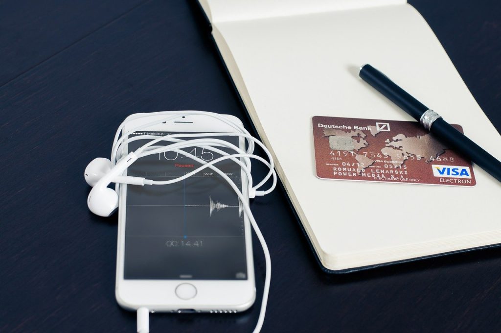 Photo of a phone beside a pen and pad with a credit card from someone possibly managing their online bank account for a frequent traveler.