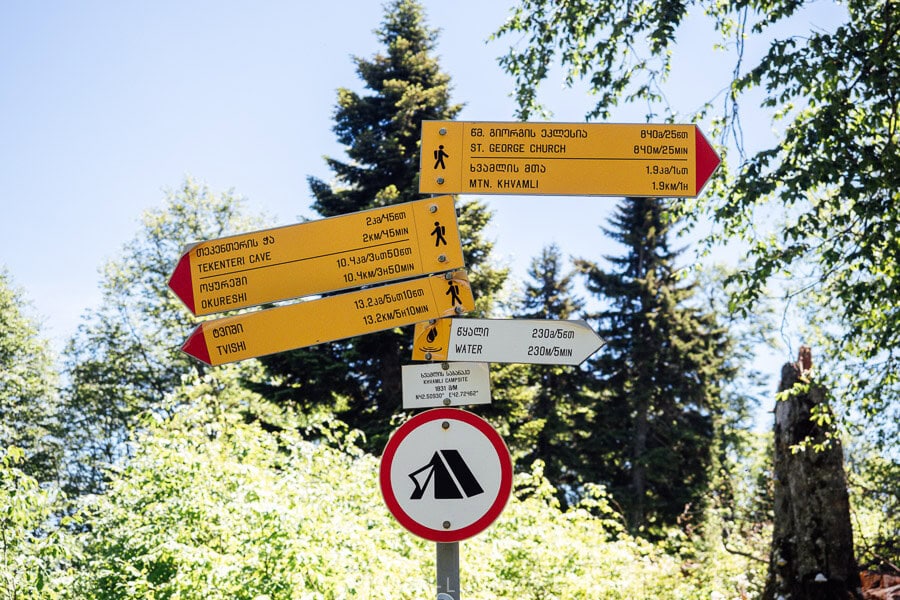 A trail sign marks the way to Khvamli Mountain peak from a camping area.