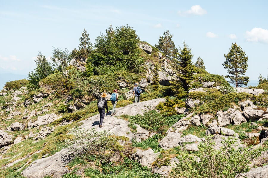 Three people walk across a rock formation towards the peak of Mount Khvamli.