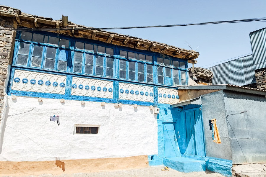 A white and blue house in Azerbaijan with floral balconies and an old roof.