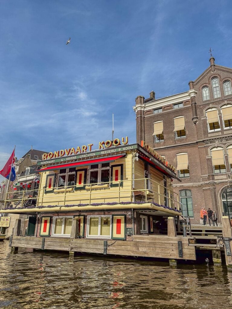 Experience Rondvaart Koou boat tour dock on Amsterdam's iconic canals with Dutch architecture and clear blue skies.