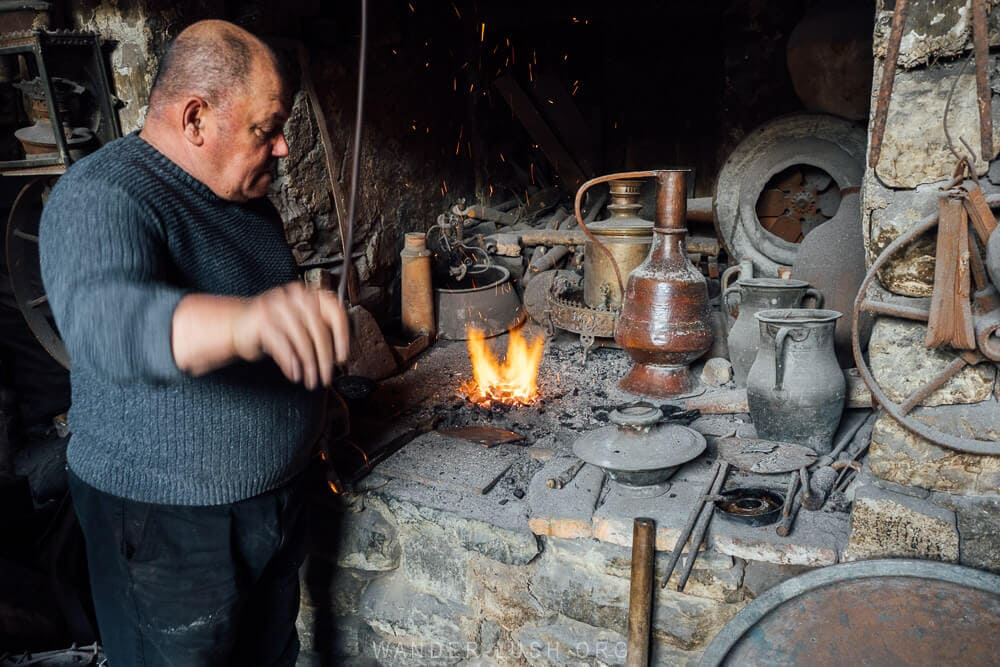 A man in a sweater uses a bellows to fan a flame inside his copper workshop in Lahic, Azerbaijan.