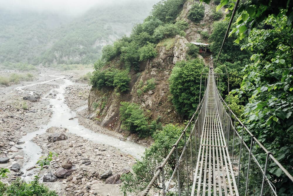 The Zarnava Hanging Bridge, a suspended rope bridge over a green river valley outside Lahic in Azerbaijan.