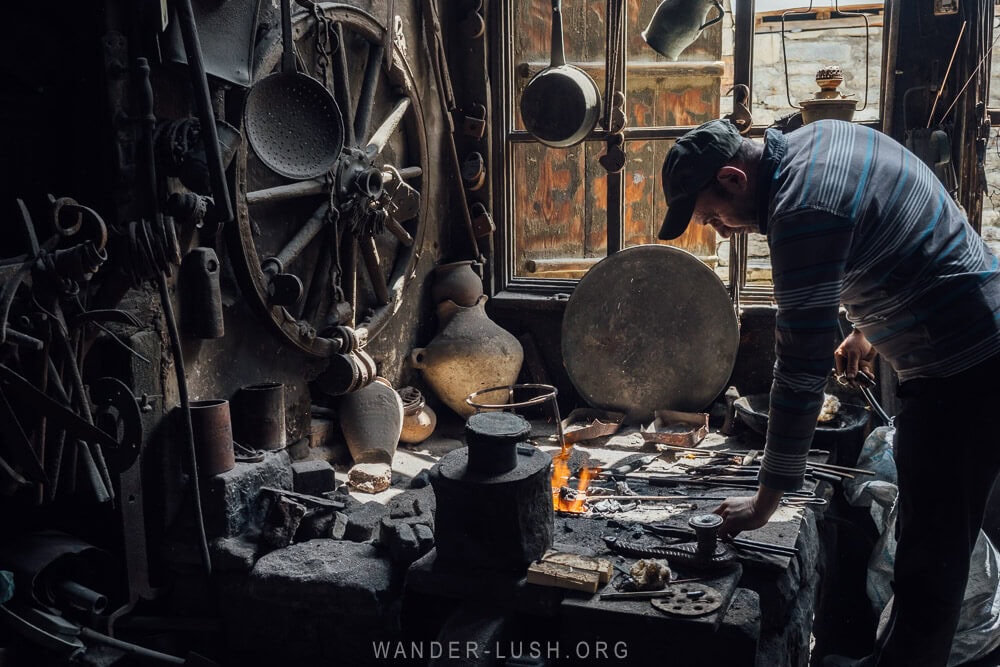 A man bends over his worktable strewn with tools and other items inside an artisan workshop in Azerbaijan.