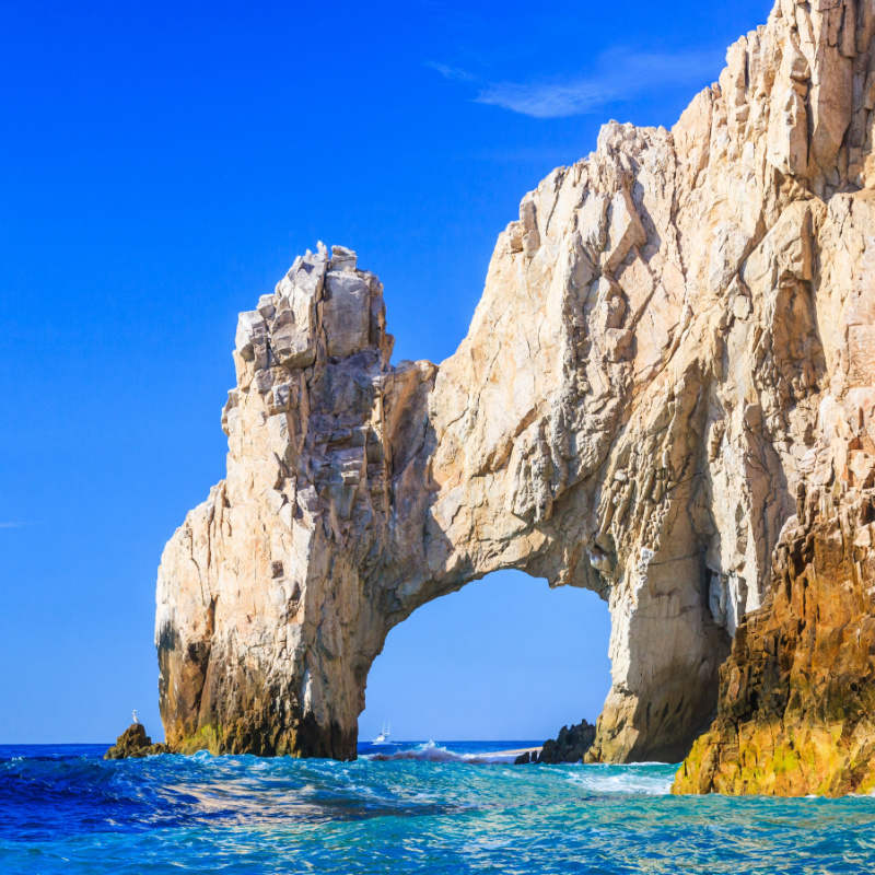 A beautiful arched rock formation frames the blue sky and clear waters in the popular tourist destination of Cabo San Lucas