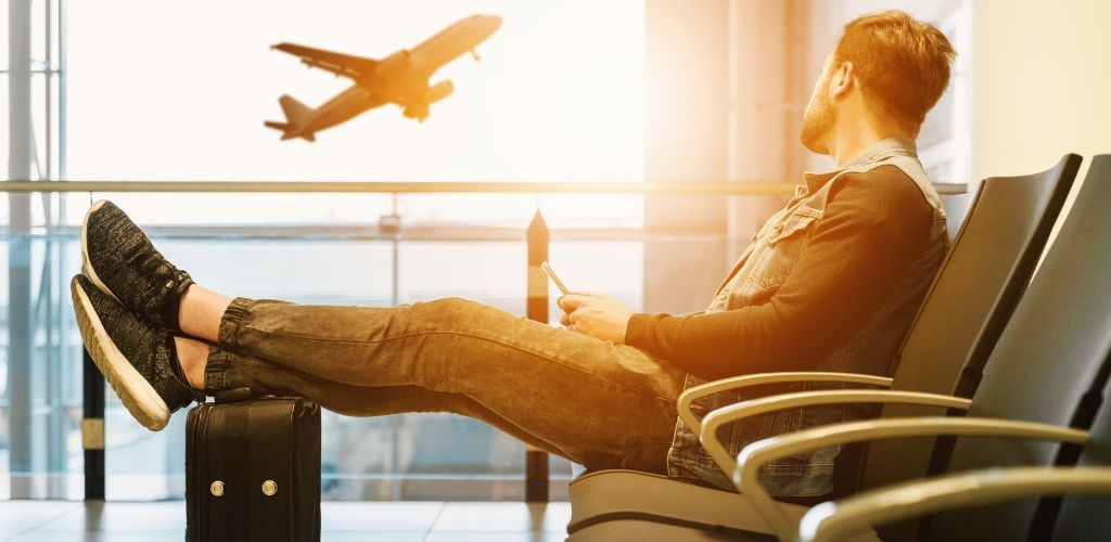 Man in airport waiting for boarding on plane, aeroplane taking off in background 