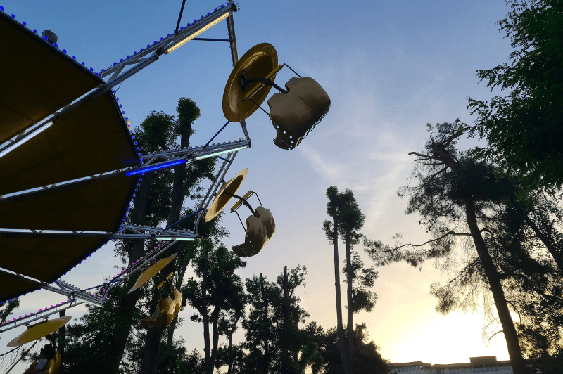 An amusement park ride spinning over head with the sun setting behind tall trees in Sunny Beach Bulgaria