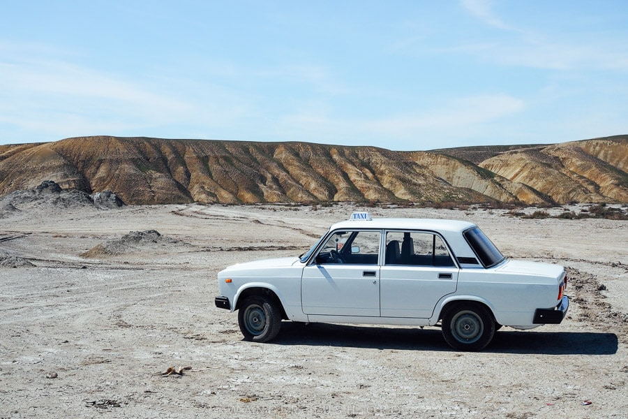 A retro white car parked in front of a landscape of mud volcanoes in Gobustan, Azerbaijan.