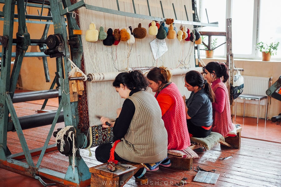 Four women weave a carpet on an upright loom.