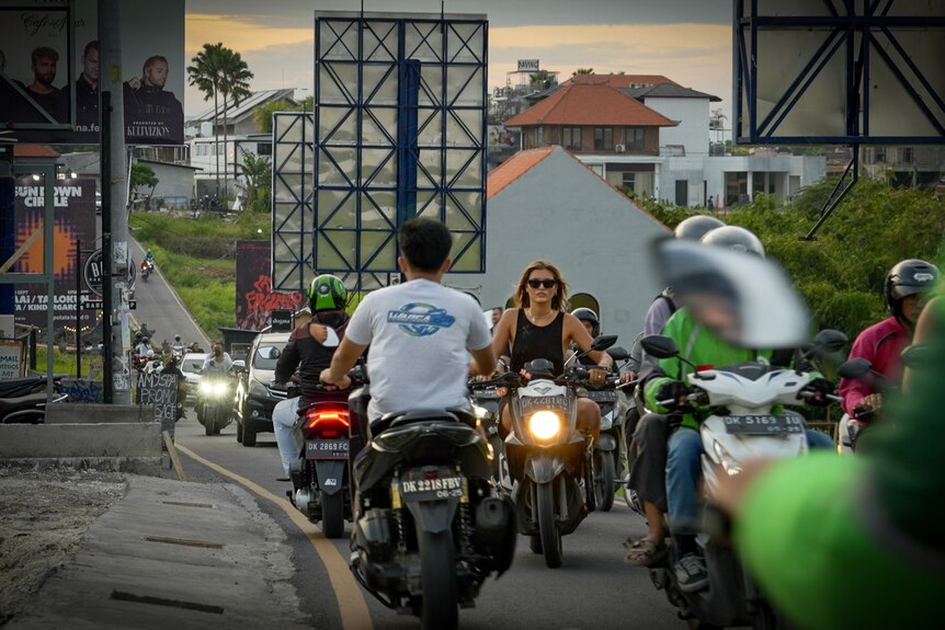 A young blonde woman rides a scooter down a busy road