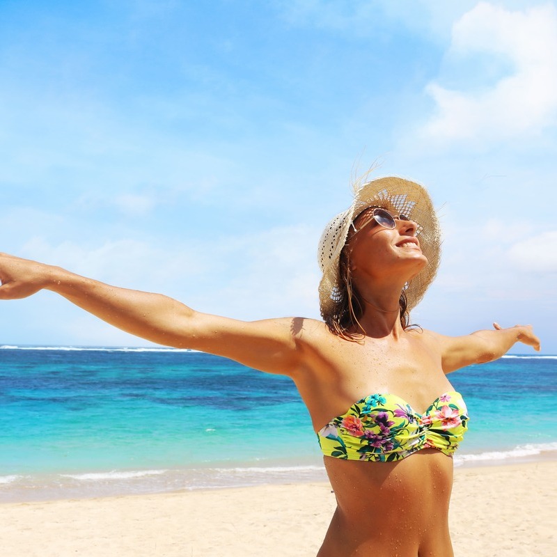 Young Woman With Her Arms Wide Open As She Enjoys A Sunny Day At The Beach In A Tropical Location