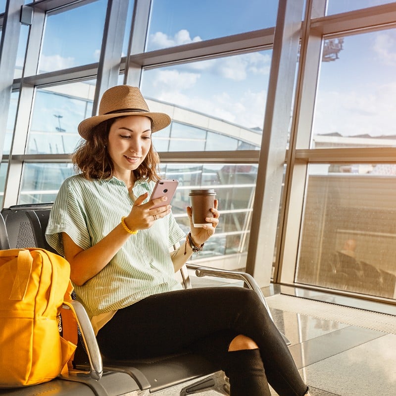 Young Female Traveler Smiling As She Checks Her Phone At An Airport