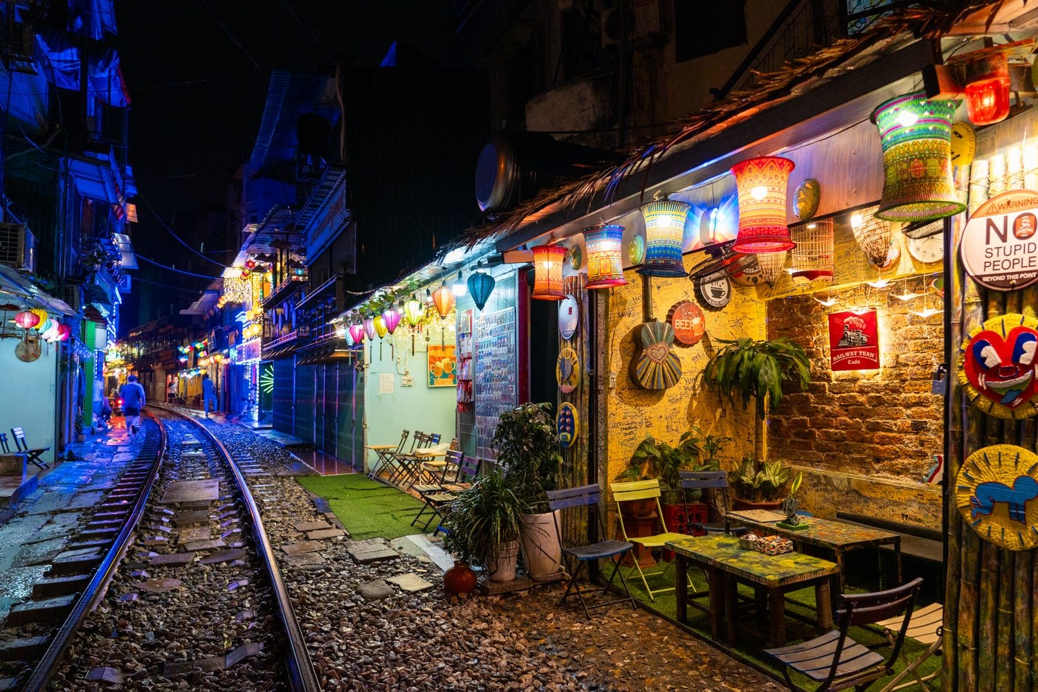 Narrow street with railroad tracks lined with cafes and shops.