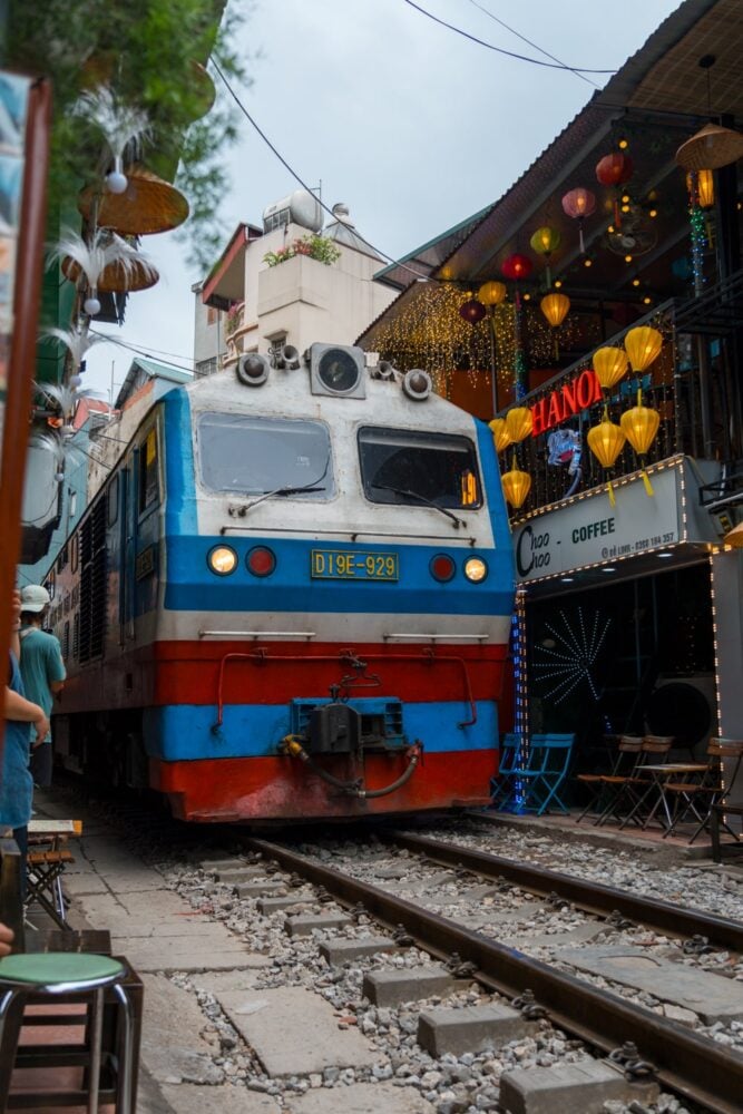 Vintage train on railroad tracks in between a narrow street lined with shops and cafes.