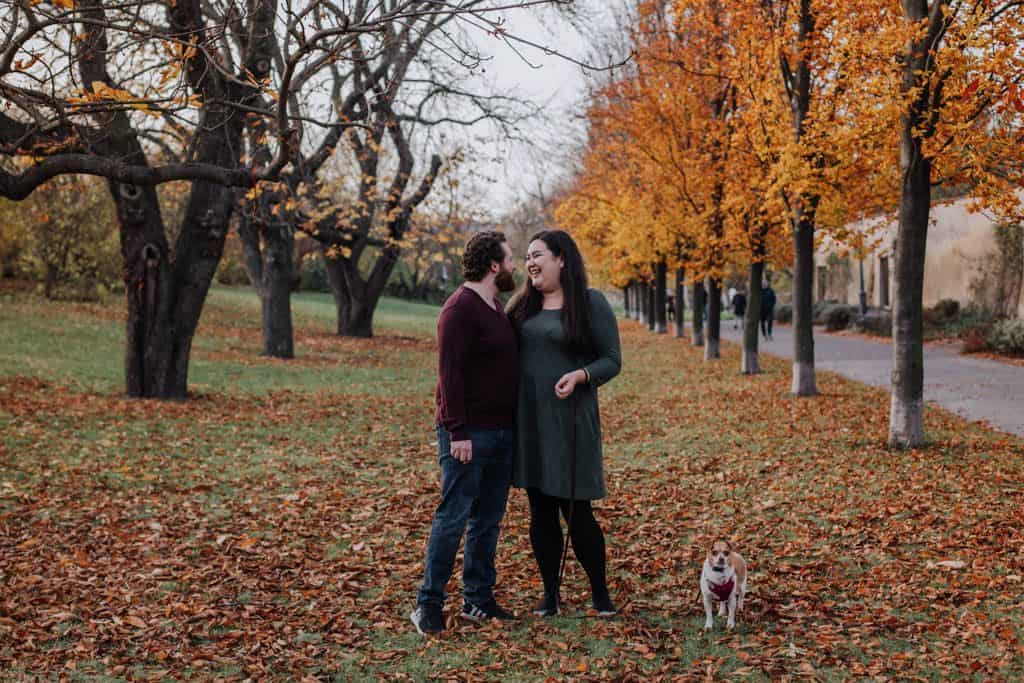 Riana, Colin and their dog, Ellie, posing Family Photos in Prague at Vysehrad Castle with fall foliage behind them