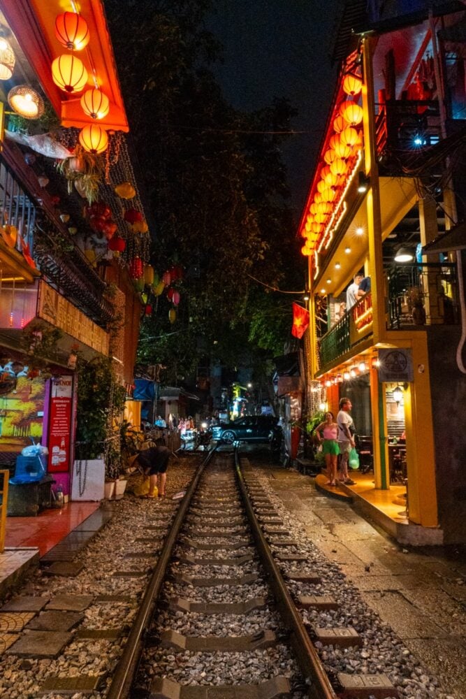 Railroad tracks and cafes and shops lit up at night on Hanoi Train Street.