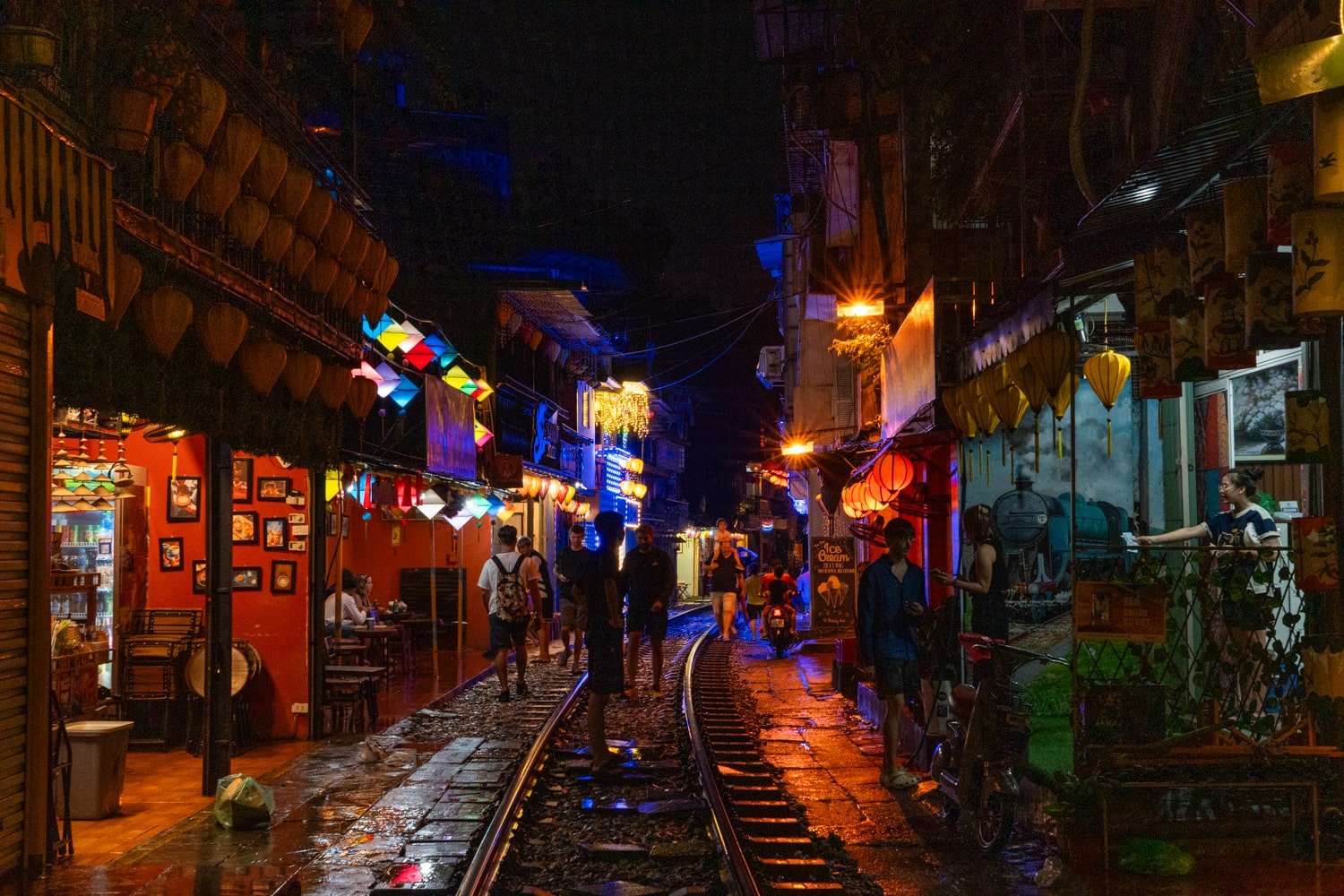 Railroad tracks and cafes and shops lit up on a rainy night on Hanoi Train Street.