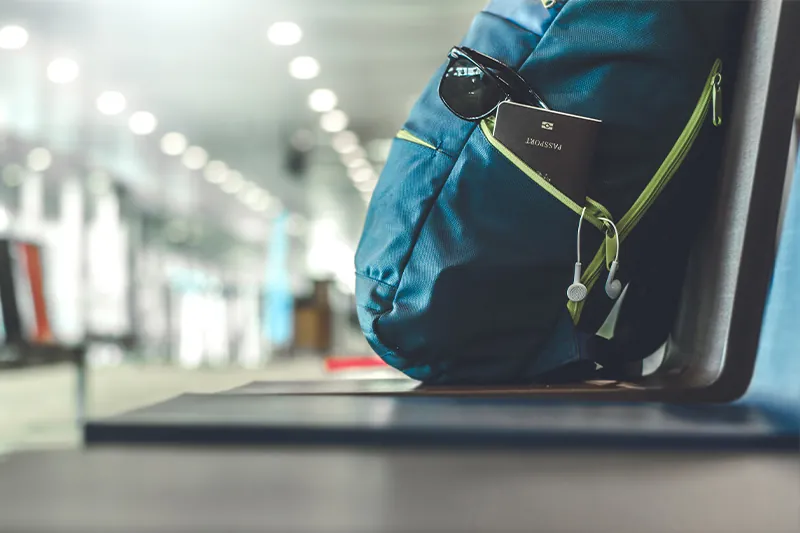 Backpack with sunglasses and passport sitting on chair at airport