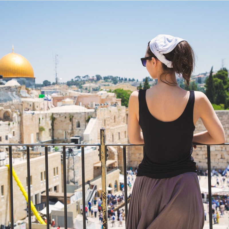 a woman looks down from a balcony into a busy square in Jeruselam