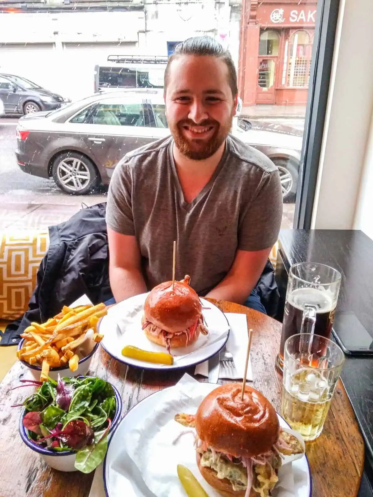 Colin sitting at a pub table in Ireland with a burger and fries in front of him 