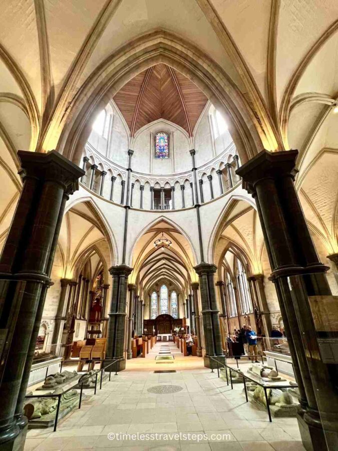 Interior view of Temple Church, highlighting its distinctive round nave and Gothic arches. The medieval architecture features intricately carved stone details, historic effigy tombs of Knights Templar, and beautiful stained glass windows, creating a solemn and historic atmosphere.
