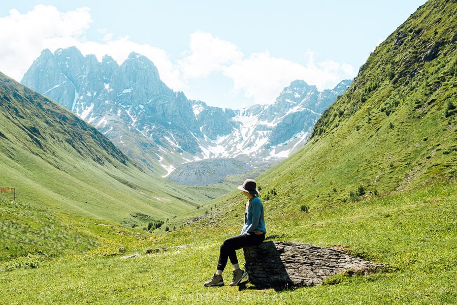 A woman sitting on a rock in a green valley in the Greater Caucasus mountains of Georgia.