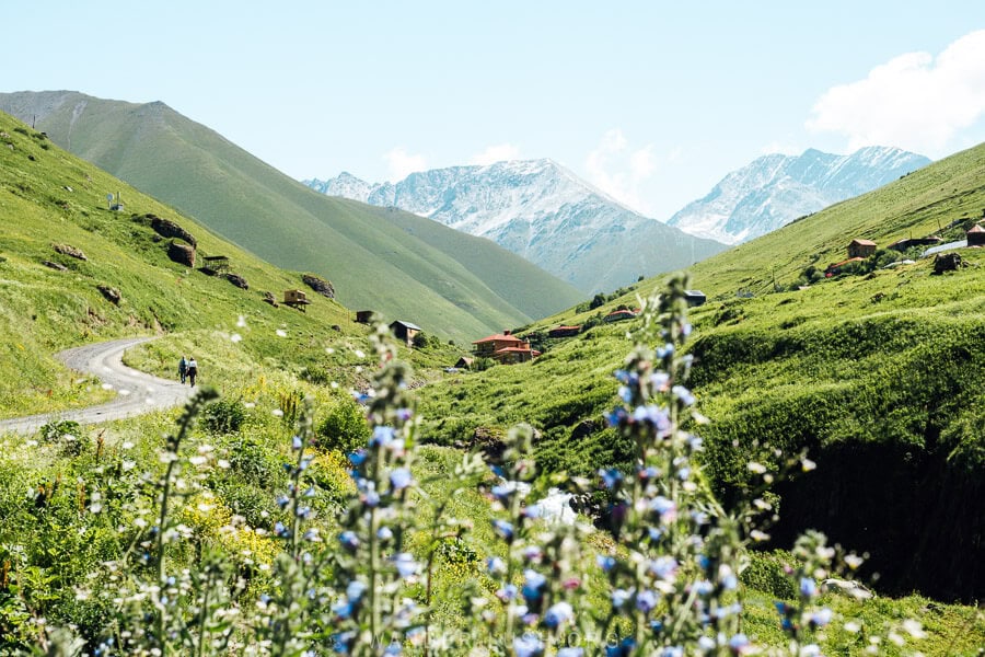 Two women walk along a winding mountain road towards Juta village.