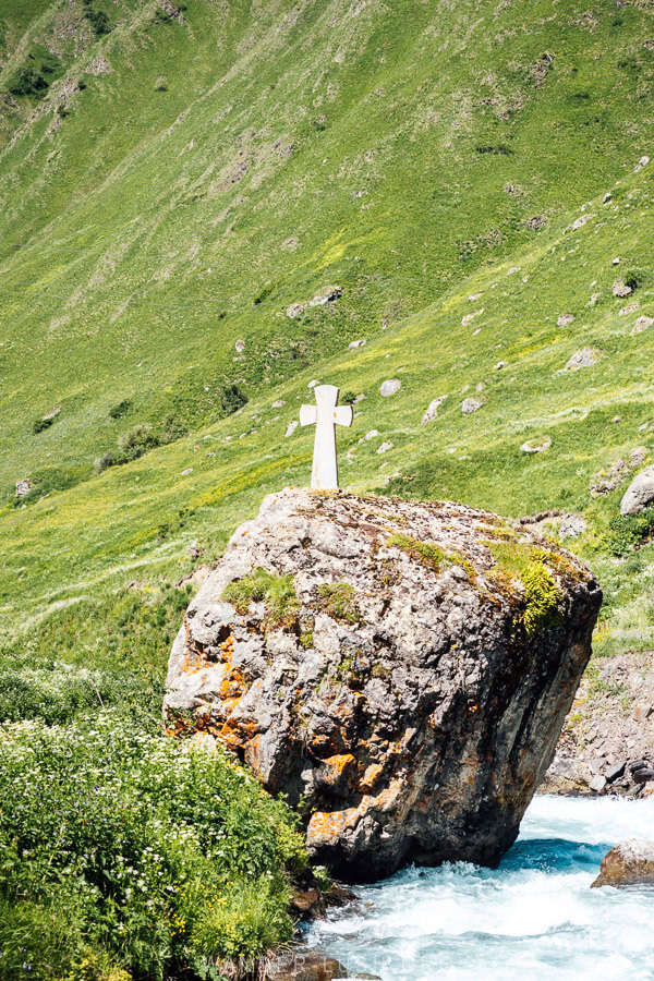 A giant stone boulder with a white cross on top in the river in Juta, Georgia.