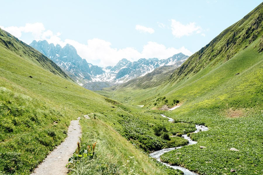 A clear trail follows a meandering river through the Juta Valley towards Chaukhi mountain.