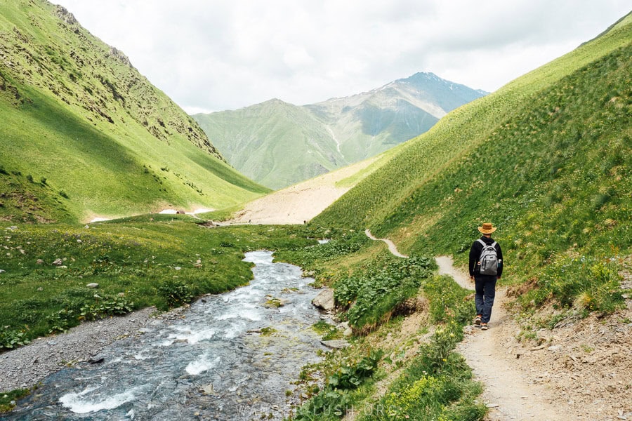 A man walking down a narrow trail along a river towards Fifth Season and Juta village.