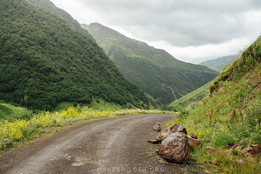 Big boulders on the side of the road from Kazbegi to Juta, with tall mountains and yellow wildflowers all around.