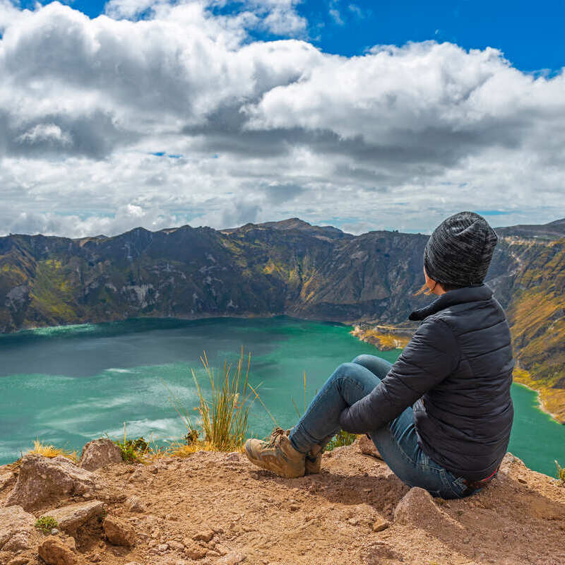 Female Tourist Posing For A Picture Overlooking A Turquoise Water Lagoon, Volcanic Formation In Ecuador