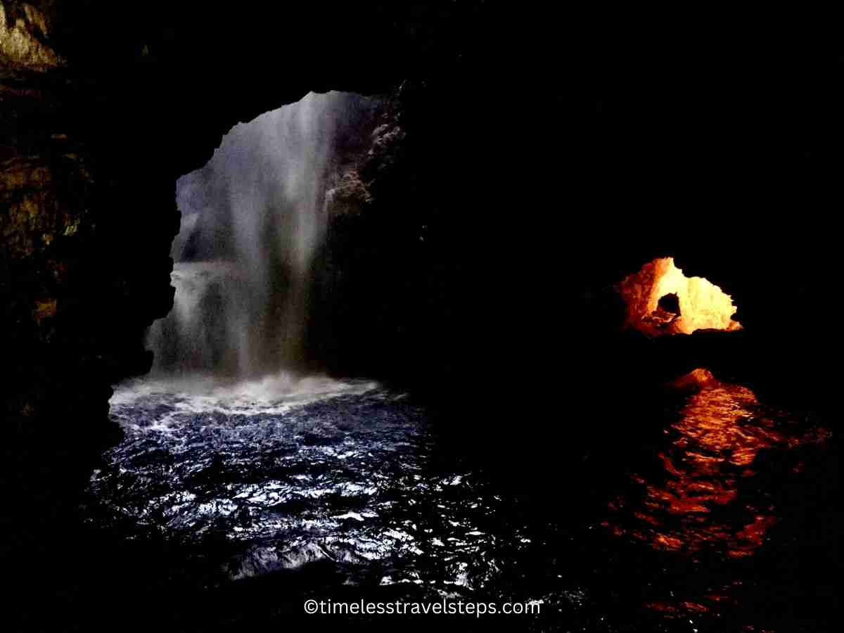 Image of the Smoo Cave waterfall with golden light seeping through an opening above, illuminating the cavern and creating a magical, ethereal atmosphere.
