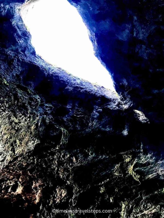 Skylight openings in the limestone roof of Smoo Cave, allowing shafts of natural light to penetrate the darkness below. The light highlights the rugged texture and intricate formations of the limestone, casting an ethereal glow and creating a striking contrast between the illuminated areas and the shadowy recesses of the cave.
