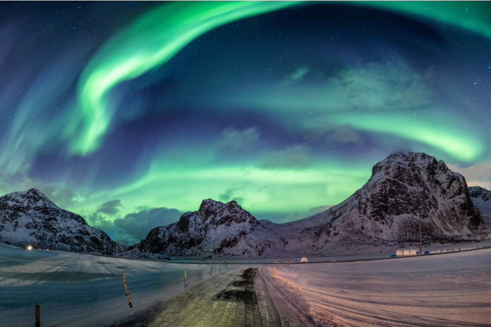 Northern lights explosion on snowy mountain range near coastline at Lofoten islands, Norway