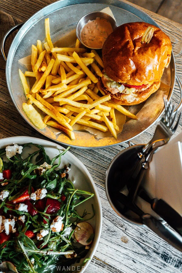 A burger with fries and a green salad on a cafe table at Rooms Kazbegi.