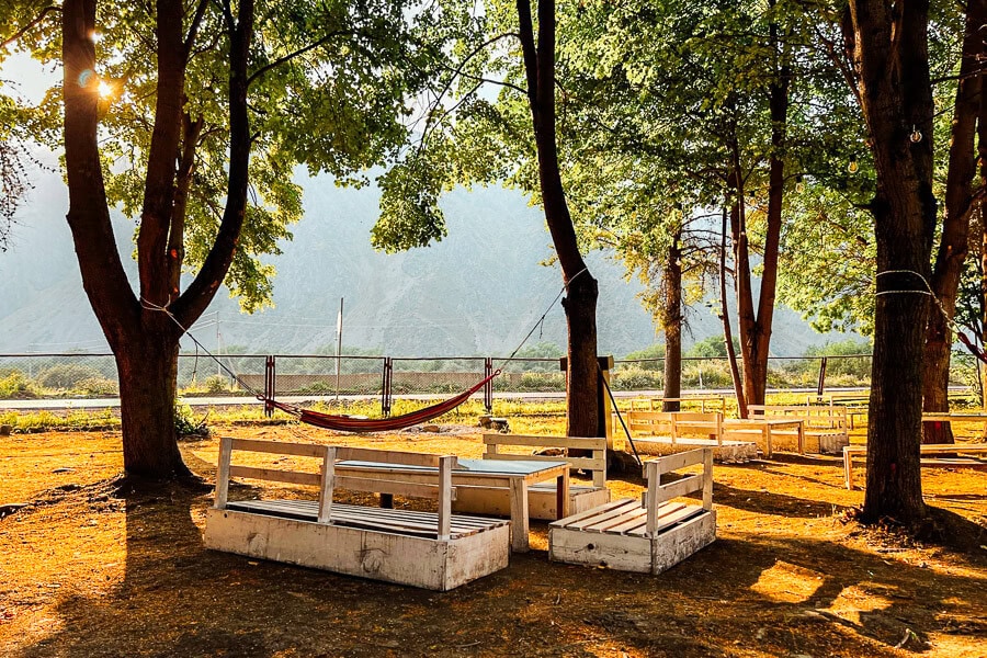 An outdoor cafe-bar near Kazbegi with wooden seats and hammocks strung between trees on the riverside.