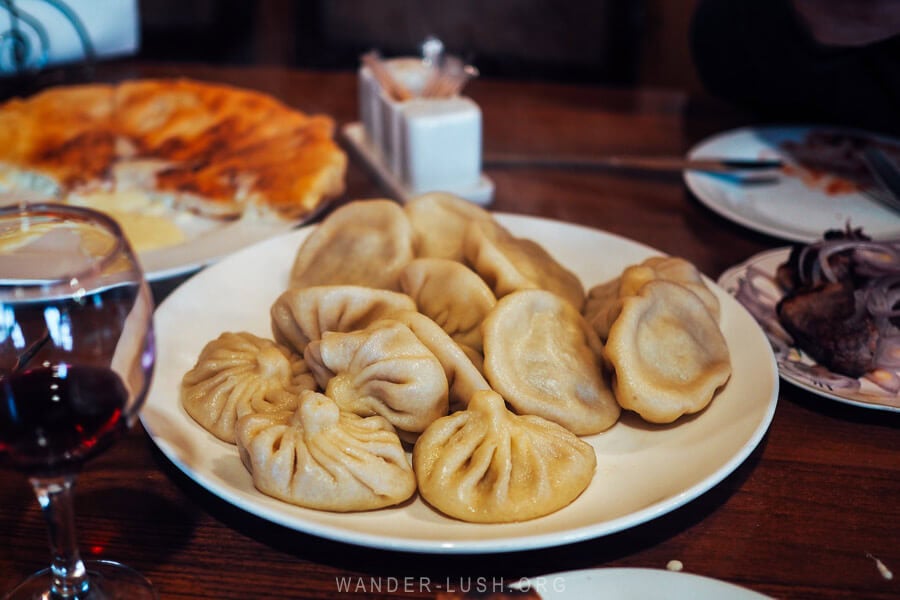 A plate of khinkali dumplings on a table surrounded by khachapuri and wine at a simple restaurant in Pasanauri village on the way to Kazbegi.