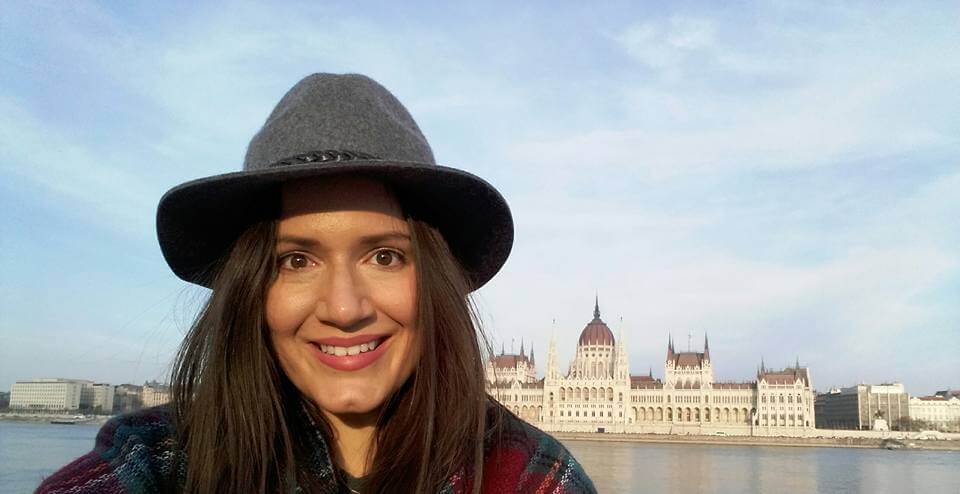 Woman in a gray hat standing in front of the parliament building in Budapest.