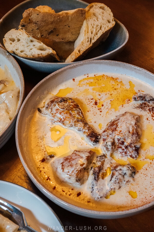 A large clay dish of chicken in garlic sauce with a side of shoti bread in Tbilisi.