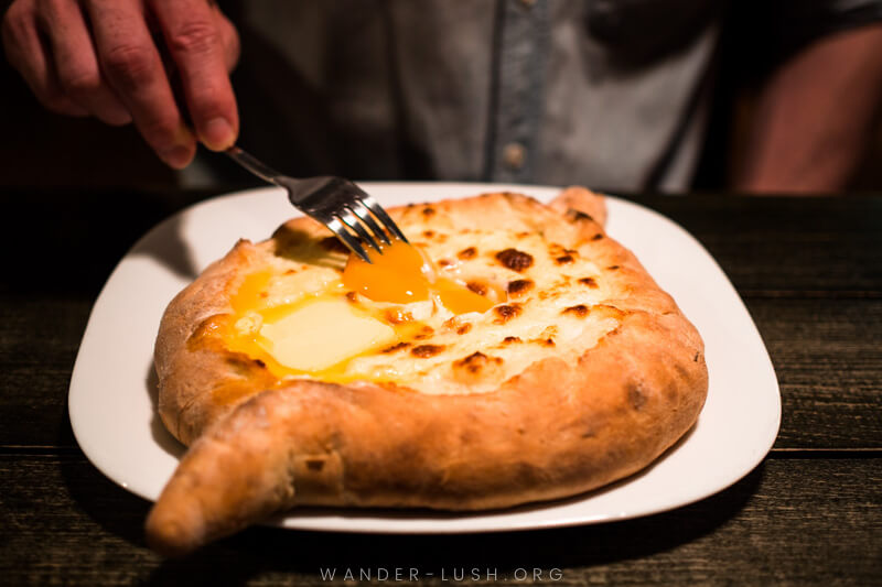 A man stirs an egg and butter into a khachapuri Adjaruli at Retro in Tbilisi.