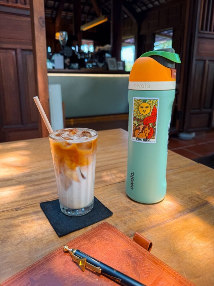 Iced coffee, water bottle, and journal on table at Café Slow in Tra Que Vegetable Village near Hoi An, Vietnam.