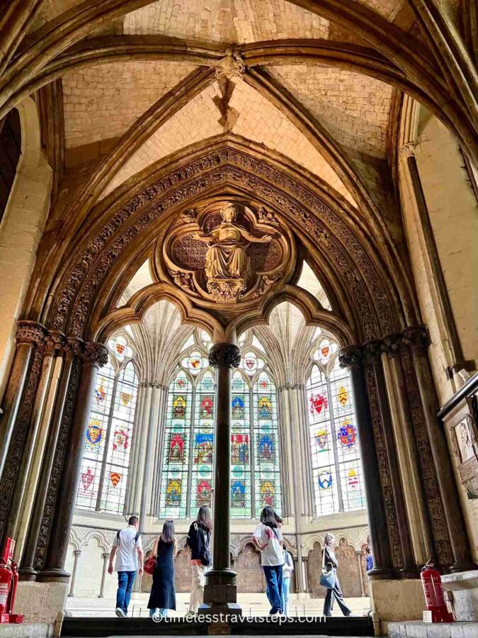 Image of the arched entrance to the Chapter House at Westminster Abbey. As you ascend the stairs, the stained glass windows and intricate carvings become visible, highlighting the Gothic architectural details and the artistry of the medieval craftsmen.
