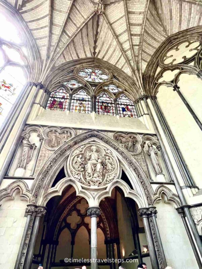 Image of the entrance to the Chapter House at Westminster Abbey, as seen from the inside. The arched doorway frames the view, showcasing the stained glass windows and detailed carvings that adorn the entrance, reflecting the grandeur of Gothic architecture.
