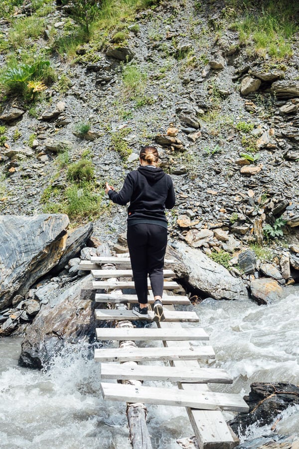 A woman crosses a wooden bridge over a river in Khevsureti.